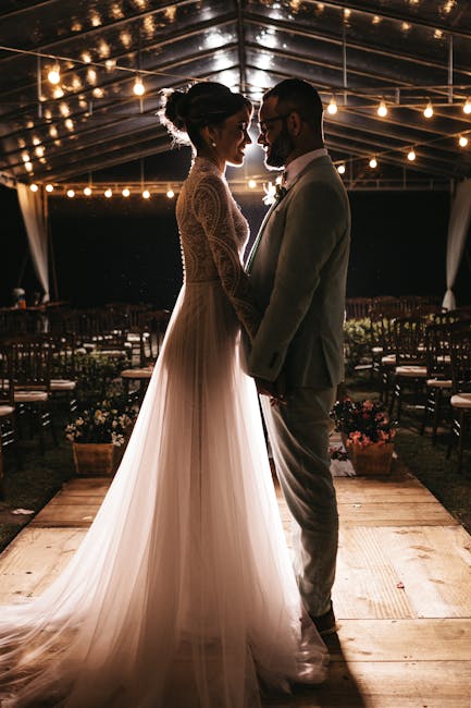 Elegant bride and groom embracing under twinkling string lights, capturing a romantic moment.